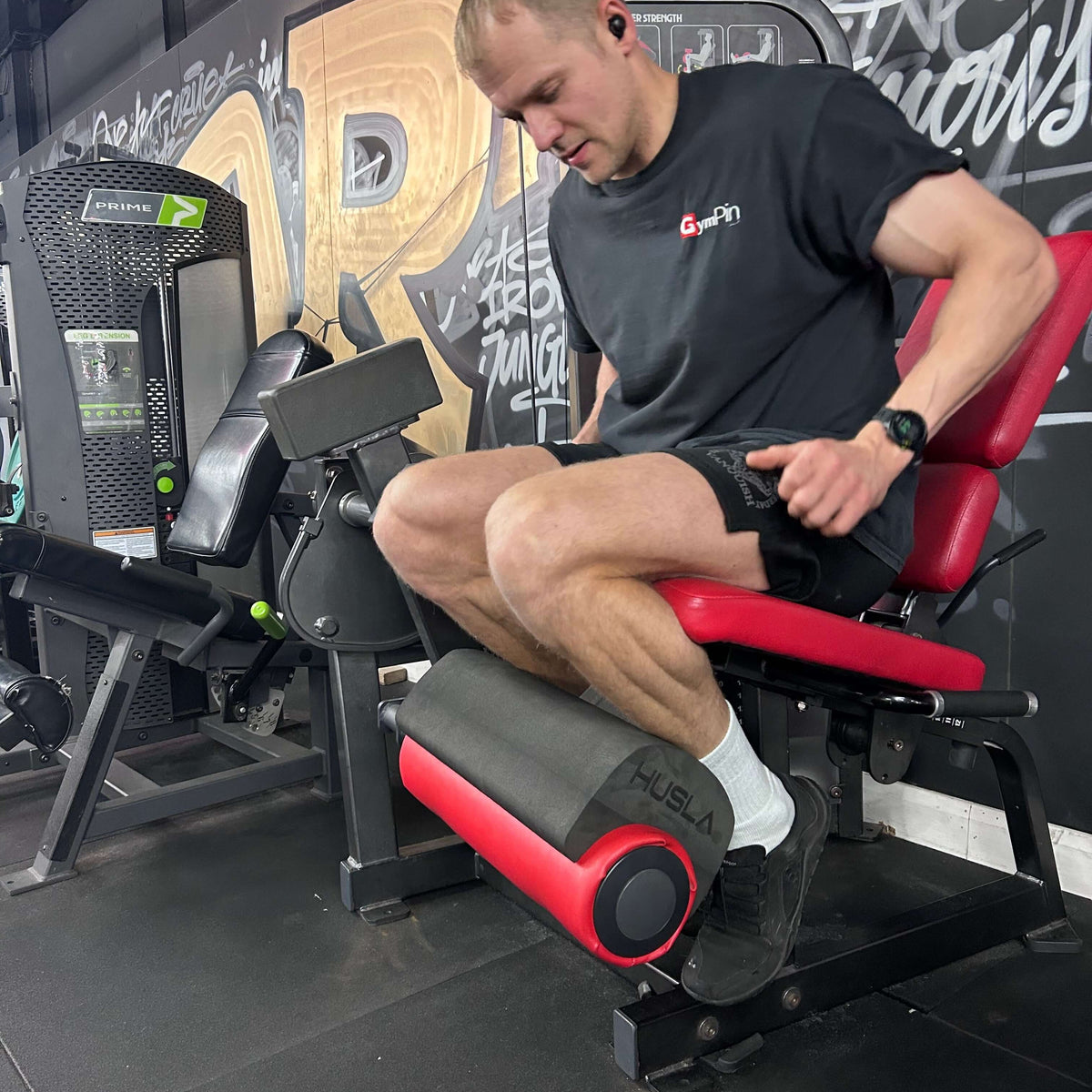 Ben from GymPin using a leg press machine in a gym with graffiti on the wall. Using a Husla Pad.