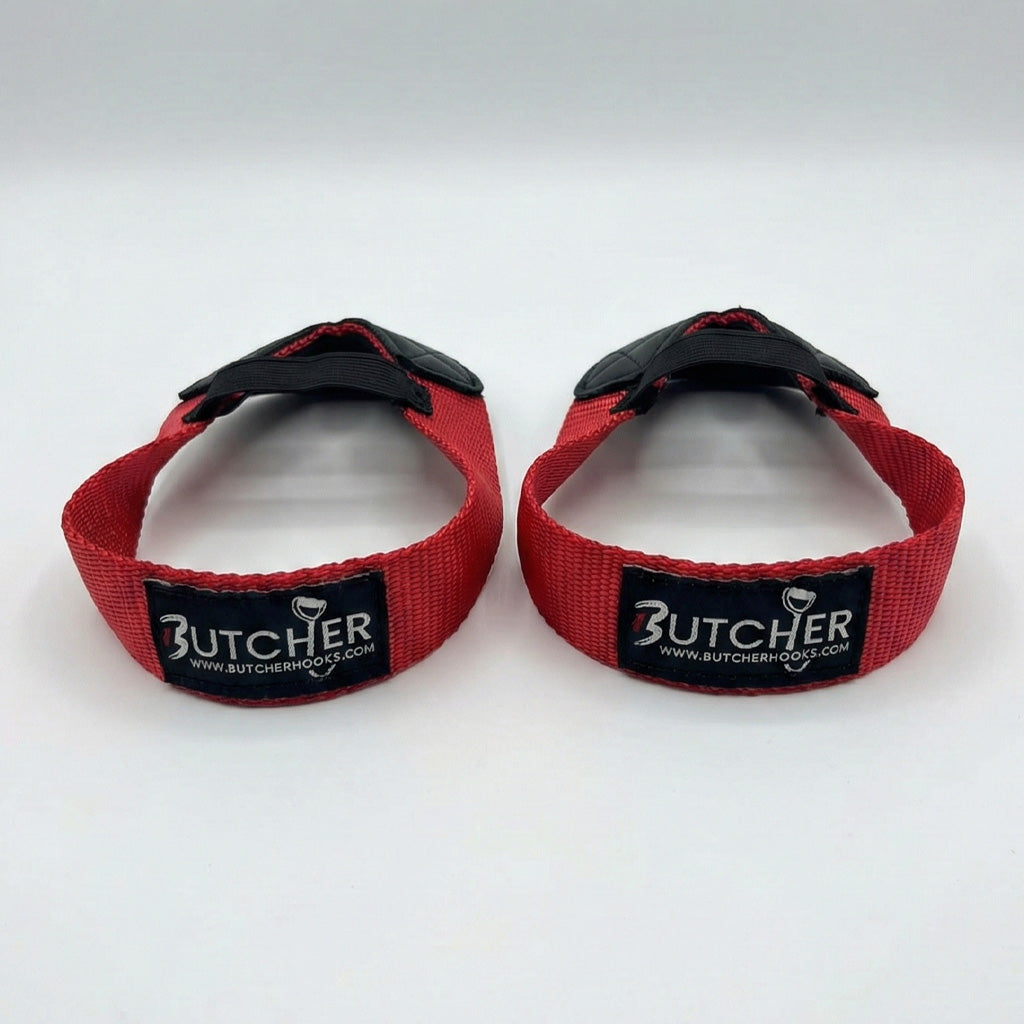 Pair of red Butcher Hooks weightlifting straps with black rubber hooks and stitched Butcher branding, designed for improved grip and support during heavy lifting.