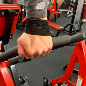 Hand wearing a black wrist support with 'GymPin' branding on a gym machine.