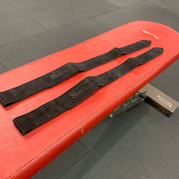 Two black weightlifting straps on a red weight bench in a gym setting.
