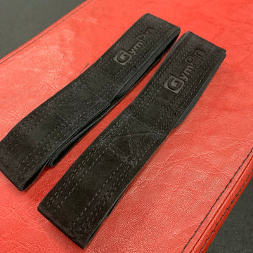 Two black leather straps with a brand logo on a red surface