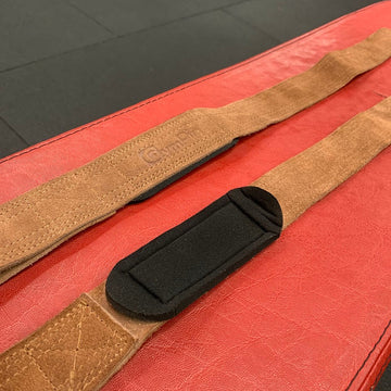 Brown guitar strap with black buckle on a red surface
