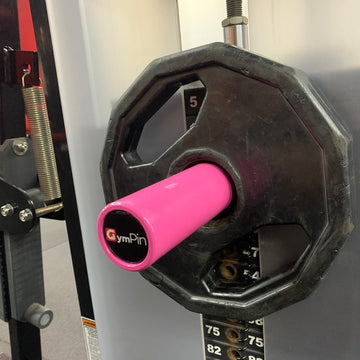 A pink GymPin attached to a weight stack in a gym, designed to hold Olympic plates for adjusting weight on a cable machine.
