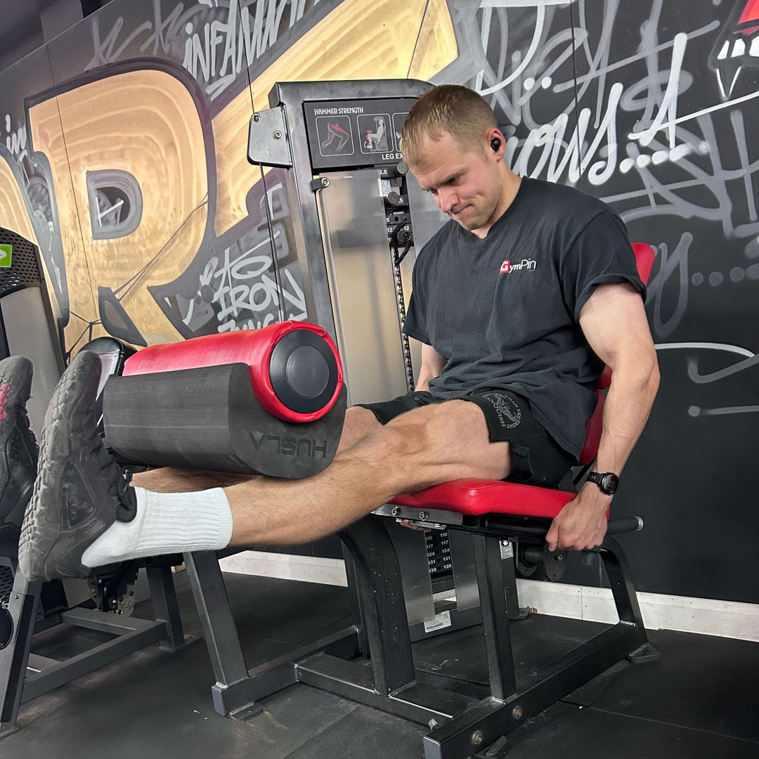 Person using a leg press machine in a gym setting with graffiti on the wall.