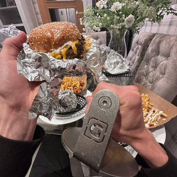 Person holding a burger and fries with a keychain in a casual indoor setting