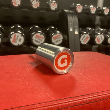 GymPin MiniPin with a red 'G' logo on a red surface, with more valve caps in the background.