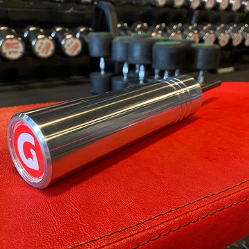 The largest GymPin, the KingPin with a red and white 'G' logo on a red surface, with weight plates in the background.