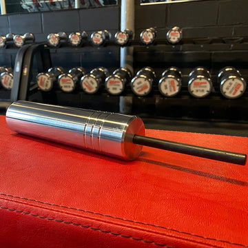 The Gympin KingPin with the coated 10 mm diameter pin on a red surface, with a row of weights in the background of the gym.
