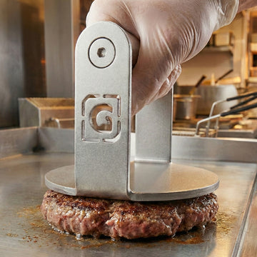 Hamburger patty being pressed with a metal tool in a kitchen setting