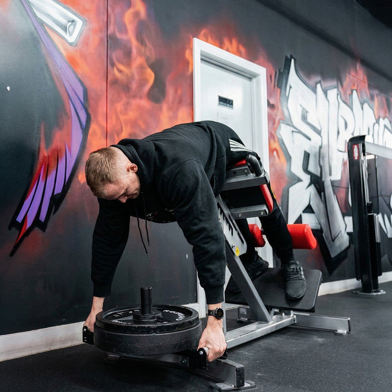 Person adjusting weights on Hyper Loader with a colorful mural in the background