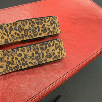 Two leopard print straps on a red leather surface